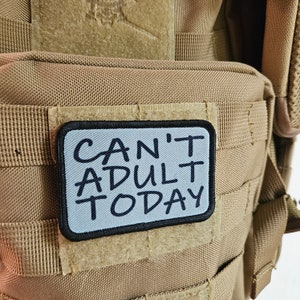 May include: A tan fabric backpack with a black and white patch that says "Can't Adult Today".