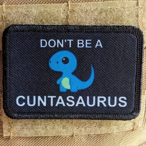 May include: A black patch with white text that reads "Don't be a Cuntasaurus". A cartoon blue dinosaur with yellow accents is in the center of the patch.