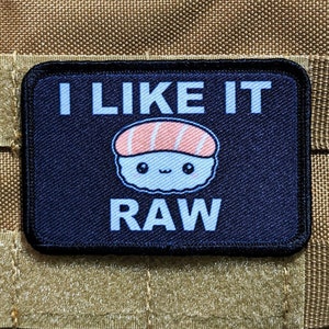 Puede incluir: Un parche bordado negro y azul con un rollo de sushi de dibujos animados y el texto "I LIKE IT RAW".