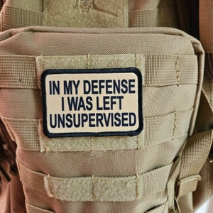 May include: A tan tactical backpack with a black patch that reads "In my defense I was left unsupervised".