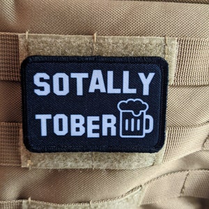 May include: A black patch with white text that reads "Sotally Tober" and a white beer mug icon.