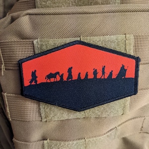 Könnte beinhalten: Ein sechseckiger Patch in Schwarz und Rot mit einer Silhouette einer Gruppe von Figuren, die über einen roten Hintergrund laufen. Die Figuren laufen in einer Reihe, und der Hintergrund ist einfarbig rot. Der Patch ist aus einem weichen, strapazierfähigen Material gefertigt und hat einen Klettverschluss.