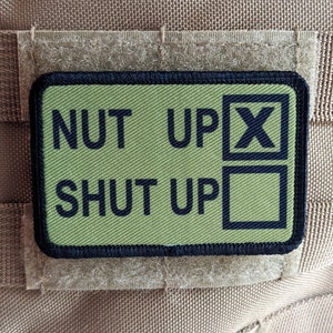 May include: Green and black patch with the text "NUT UP X SHUT UP" in black lettering.