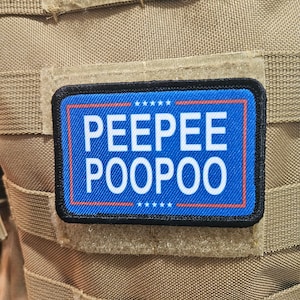 Può includere: Una toppa blu e rossa con testo bianco che recita "PEEPEE POOPOO" su uno sfondo beige.