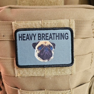 Könnte beinhalten: Ein beiger taktischer Rucksack mit einem schwarzen Patch, auf dem "Heavy Breathing" steht und ein Mops mit blauen Augen abgebildet ist.