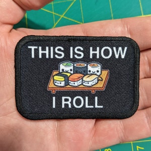 Puede incluir: Parche negro con texto blanco que dice "This is how I roll" y una imagen de dibujos animados de rollos de sushi en un plato.