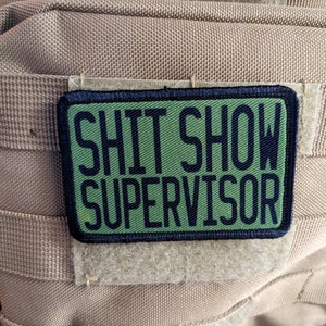 Puede incluir: Un parche verde y negro con el texto "SHIT SHOW SUPERVISOR" en letras negras.