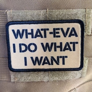 Op de afbeelding: Een beige patch met zwarte stiksels en de tekst "WHAT-EVA I DO WHAT I WANT" in zwart.