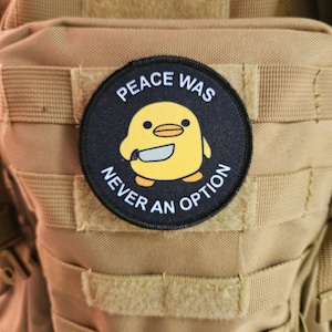 Peut inclure: Un patch noir et blanc avec un poussin de dessin animé jaune tenant un couteau. Le texte sur le patch est "Peace Was Never An Option."
