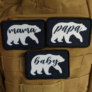 May include: Three black fabric patches with white bear silhouettes and the words "mama", "papa", and "baby" in white cursive font.