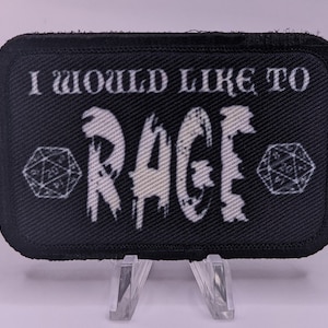May include: Black fabric patch with white text that reads "I would like to Rage" with a stylized white image of a dice on each side of the text.