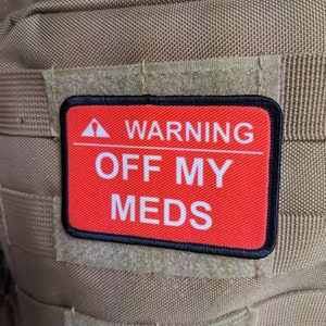 May include: A red patch with black trim and white text that reads "WARNING OFF MY MEDS" with a small triangle symbol above the word "WARNING".