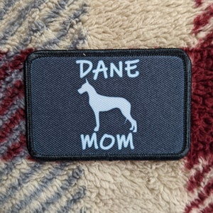 Może przedstawiać: Czarny patch z białym tekstem "DANE MOM" i białą sylwetką doga niemieckiego.