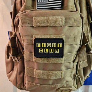 Peut inclure: Un sac &agrave; dos tactique beige avec un patch drapeau am&eacute;ricain noir et blanc et un patch noir avec des lettres jaunes qui disent "FIGHT CLUB".