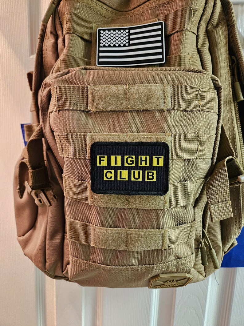 Peut inclure: Un sac &agrave; dos tactique beige avec un patch drapeau am&eacute;ricain noir et blanc et un patch noir avec des lettres jaunes qui disent "FIGHT CLUB".