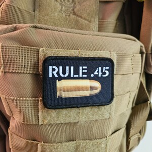 May include: A black patch with white text that reads "RULE .45" and a gold-coloured bullet on a tan tactical vest.