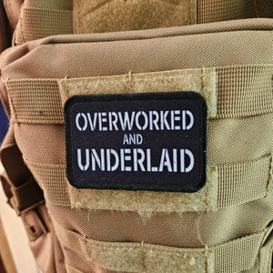 May include: A tan tactical backpack with a black patch that reads "Overworked and Underlaid".