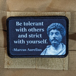 Könnte beinhalten: Ein rechteckiger Aufnäher mit schwarzem Rand und dem Zitat "Sei tolerant gegenüber anderen und streng zu dir selbst", das Marcus Aurelius zugeschrieben wird. Der Aufnäher zeigt ein blau getöntes Porträt von Marcus Aurelius.