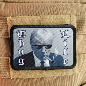 Puede incluir: Un parche bordado en blanco y negro con un hombre que lleva gafas de sol y un cigarro. El texto "Thug Life" está en el lado izquierdo del parche y "Little" en el lado derecho.