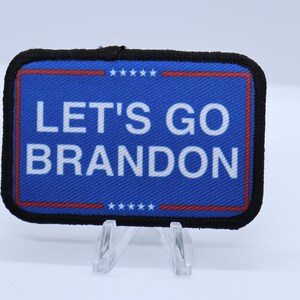 May include: A blue and black fabric patch with the text "LET'S GO BRANDON" in white. The patch has a red and white border with stars.