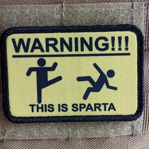Peut inclure: Un panneau d'avertissement jaune avec du texte et des graphiques noirs. Le panneau indique "WARNING!!!" et "THIS IS SPARTA". Les graphiques représentent un bonhomme bâton qui donne un coup de pied et un bonhomme bâton qui tombe.