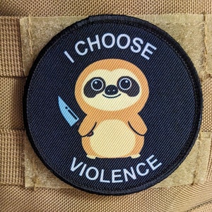 May include: A black and white round patch with a cartoon sloth holding a knife. The text "I CHOOSE VIOLENCE" is written around the sloth.