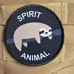 以下が含まれることがあります： 漫画のナマケモノと「SPIRIT ANIMAL」というテキストが刺繍された黒と白のワッペンです。