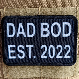 Puede incluir: Parche negro con texto blanco que dice "DAD BOD EST. 2022".