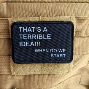 May include: Black patch with white text that reads "That's a terrible idea!! When do we start?" The patch is attached to a tan molle panel.