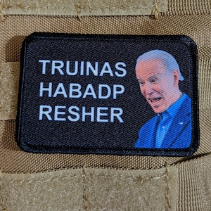 Peut inclure: Un patch noir avec du texte blanc qui dit "TRUINAS HABADP RESHER" et une photo de Joe Biden en costume bleu.