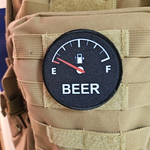 Peut inclure: Un patch noir et blanc avec une jauge de carburant qui indique "E" pour vide et "F" pour plein. L'aiguille pointe vers "E". La jauge est étiquetée "BEER".