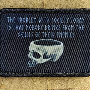May include: Black patch with white text that reads "THE PROBLEM WITH SOCIETY TODAY IS THAT NOBODY DRINKS FROM THE SKULLS OF THEIR ENEMIES". A white skull with a hollowed-out top is depicted below the text.