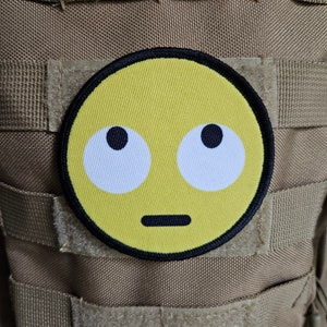 May include: A yellow embroidered patch with a black outline, depicting a cartoon face with wide eyes and a neutral expression.