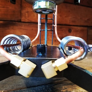 May include: A close-up of a steampunk-style coffee maker with copper pipes, a black metal base, and a silver filter. The coffee maker has a knob for adjusting the pressure and a ladder-like structure.
