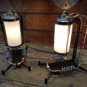 May include: Two steampunk-style table lamps with a white frosted glass shade, black metal base, and copper accents. The lamps have a unique design with a coil spring and a pipe-like structure.