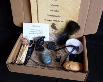 May include: A cardboard box containing The Raven Spirit Kit with a card featuring text about wisdom, protection, and transformation. Includes a glass vial of matches, a black raven figurine, a polished stone, a black feather, a candle, and a small vial.