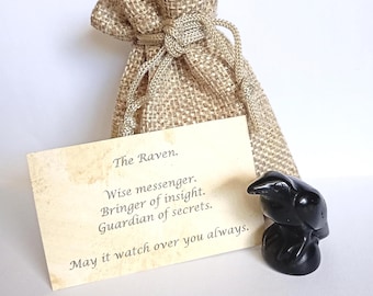 May include: A small black raven figurine carved from stone, a tan burlap drawstring pouch, and a rectangular card with the text: The Raven. Wise messenger. Bringer of insight. Guardian of secrets. May it watch over you always.