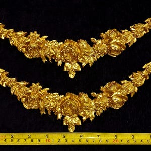 Pu&ograve; includere: Due ornamenti floreali dorati e ornati. Ogni pezzo presenta rose, foglie e altri elementi floreali. Un metro a nastro giallo &egrave; in basso, che mostra i centimetri.