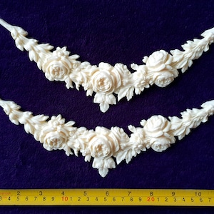 Pu&ograve; includere: Due applicazioni decorative floreali color crema. Ogni applicazione ha la forma di una ghirlanda curva, con rose e foglie dettagliate. Le applicazioni sono lunghe circa 30 cm, con un metro a nastro giallo in basso.