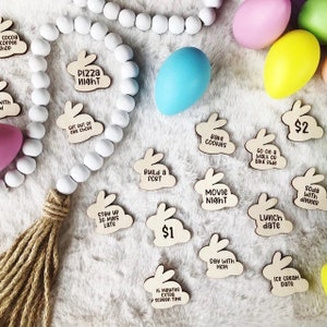 Puede incluir: Fichas de madera con forma de conejito con actividades como "Pizza Night" y "Movie Night". Est&aacute;n dispuestas con coloridos huevos de Pascua y una guirnalda de cuentas blancas.