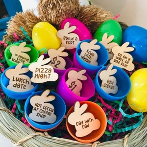 Puede incluir: Una cesta de mimbre llena de coloridos huevos de Pascua de pl&aacute;stico y etiquetas de madera con forma de conejito. Los huevos son de varios colores y las etiquetas tienen frases como "Lunch date" y "Day with Dad."