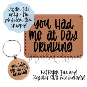 以下が含まれることがあります： 黒い文字で「You Had Me at Day Drinking」と書かれた茶色の革製のキーホルダー。キーホルダーは銀色のキーリングに取り付けられています。画像には、デジタルファイルのダウンロードに関する通知も含まれています。
