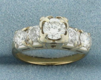 May include: A gold band engagement ring with five round diamonds. The center diamond is larger than the four surrounding diamonds.