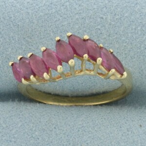 Puede incluir: Un anillo de oro con una fila de piedras preciosas de forma marquesa rosa engastadas en un diseño curvo.