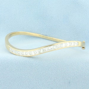 Puede incluir: Un brazalete de oro con una fila de diamantes de forma cuadrada dispuestos en forma de onda.