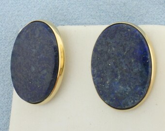 Könnte beinhalten: Ein Paar goldene Ohrringe mit ovalen Lapislazuli-Steinen. Die Steine sind tiefblau mit goldenen Flecken.