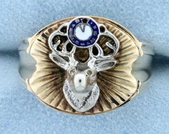 Könnte beinhalten: Ein Gold- und Silberring mit einem Hirschkopfdesign. Der Hirschkopf ist von einem blauen und weißen Emaillekreis mit einem roten Punkt in der Mitte umgeben.