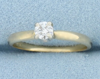 May include: A simple gold band engagement ring with a single round diamond.