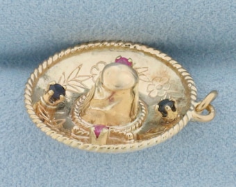 Op de afbeelding: Gouden bedel van een sombrero met rode en zwarte edelstenen. De sombrero is versierd met bloemmotieven.