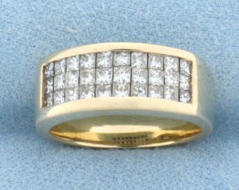 Op de afbeelding: Een goudkleurige ring met een rechthoekig ontwerp, met meerdere vierkant geslepen, heldere edelstenen. De ring heeft een brede band en een gepolijste afwerking, die een klassieke en elegante stijl laat zien.